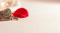 Decorative wooden heart with intricate pattern and red fabric heart on soft beige textured surface for romantic Valentine's Day celebration.