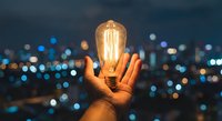 Hand holding glowing vintage Edison bulb against blurred city lights at night. Creative concept for innovation, ideas, inspiration and energy solutions.