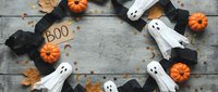 Halloween decorations with white ghosts, orange pumpkins, black bats and autumn leaves arranged in circle on rustic wooden background for spooky seasonal design.