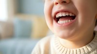 Young woman laughing joyfully showing white teeth in cozy indoor setting. Genuine happiness and positive emotions concept for wellness and lifestyle content.