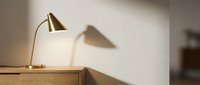 Brass desk lamp with wooden base casting shadow on white wall, modern minimalist interior design and home decor.