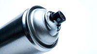 Aerosol spray can nozzle in close-up against white background, showing metal valve and trigger mechanism for painting, graffiti, or industrial applications.