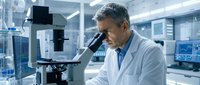 Middle-aged Caucasian male scientist in white lab coat examining samples through microscope in modern research laboratory with advanced equipment.