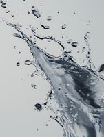 Dynamic water splash with scattered droplets captured in motion against light background, creating dramatic liquid movement and transparent fluid patterns.