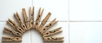 Wooden clothespins arranged in a semicircle on a white tiled surface, creating a sun or fan shape with natural wood texture.