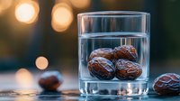 Fresh dates submerged in clear water glass with bokeh lights background creating artistic food composition with natural lighting and reflections.