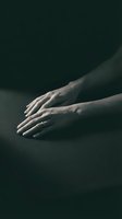 Elegant female hands with wedding ring resting on dark surface in dramatic moody lighting for luxury and romance concepts.