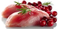 Raw meat fillets garnished with fresh rosemary sprigs and bright red cranberries on white background, showcasing gourmet food preparation ingredients.