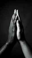 Two hands meeting in prayer or high-five gesture against dark background, symbolizing unity, agreement, partnership, teamwork, and collaboration between diverse individuals.