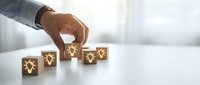 Professional hand arranging wooden blocks with glowing lightbulb icons representing innovation, creativity and business ideas on clean white surface.