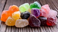 Colorful sugar coated jelly candies on rustic wooden background. Sweet gummy treats in various fruit flavors arranged in vibrant composition for confectionery.
