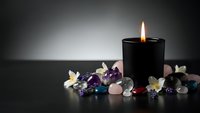 Black candle burning with healing crystals and white flowers for meditation, spa wellness, spiritual ritual and relaxation therapy.