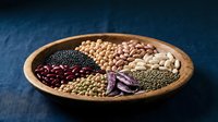 Assorted legumes and beans in wooden bowl on dark blue background for healthy cooking and nutrition concepts.