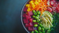 Fresh poke bowl with raw tuna, mango, edamame, avocado, carrots and seaweed arranged in colorful sections, topped with sesame seeds on dark background.