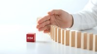 Business hand protecting wooden domino blocks from falling with red risk cube, crisis management and financial protection strategy concept.