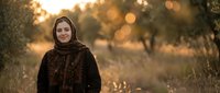 Young Middle Eastern woman in traditional headscarf smiling warmly in golden sunset light outdoors with natural bokeh background for lifestyle content.