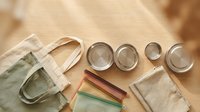 Flat lay overhead view of reusable cotton tote bag, glass storage jars, and natural linen cloths arranged on neutral beige background for sustainable living and eco-friendly lifestyle content.