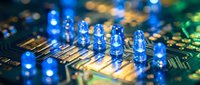 Glowing blue light-emitting diodes mounted on golden circuit board traces with shallow depth of field, representing technology, electronics, and semiconductor manufacturing for industrial and tech design projects.