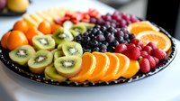Fresh colorful fruit platter with sliced oranges, kiwi, strawberries and grapes arranged on black plate for healthy eating and party catering.