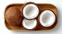 Fresh coconuts arranged on wooden tray showing whole and halved tropical fruits with white flesh exposed for healthy cooking and natural ingredients.