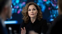 Professional woman with wavy brown hair wearing black sparkly outfit gestures during business meeting against blurred blue and pink bokeh background. Confident executive pose.