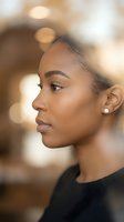 Young African American woman in profile with natural makeup and earrings against warm bokeh background for beauty and lifestyle concepts.