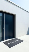 Modern minimalist home entrance with dark blue door and welcome mat on concrete floor, conveying hospitality and contemporary architecture.