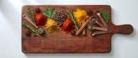 Colorful spices and herbs arranged on rustic wooden cutting board with cinnamon sticks creating vibrant culinary display for cooking and seasoning recipes.