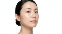 Young Asian woman with natural makeup and sleek hair bun on white background, skincare and beauty concept for cosmetic advertising and wellness campaigns.
