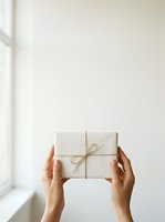 Hands holding wrapped gift box with twine bow against white wall and natural window light, suitable for holiday, celebration, present giving, and seasonal marketing campaigns.