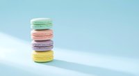 Colorful French macarons stack on pastel blue background with soft shadows. Sweet dessert cookies in mint green, pink, purple and yellow colors.