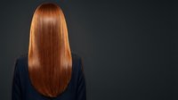 Woman with long glossy red hair viewed from behind on dark background, showcasing smooth, healthy, straight locks after salon treatment.