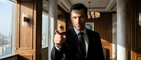 Serious businessman in dark suit pointing finger forward in modern office interior with large windows and warm lighting for corporate presentations.
