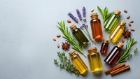 Essential oils in amber glass bottles with fresh herbs, spices and lavender arranged on white background for aromatherapy and natural wellness treatments.