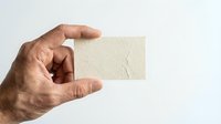 Male hand holding blank cream textured business card mockup against white background for branding design presentation and corporate identity materials.