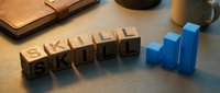 Wooden letter blocks spelling SKILL with blue ascending bar chart on desk representing professional development and career growth in business environment.