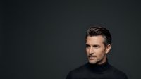 Mature Caucasian man with dark hair and facial stubble wearing black turtleneck against dark background. Professional headshot suitable for corporate, business, and portrait use.