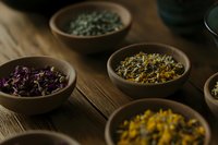 Dried medicinal herbs and flowers in wooden bowls on rustic table, moody natural lighting creates atmospheric composition for wellness and holistic healing.