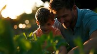 Father and son sharing tender moment outdoors during golden sunset, smiling and bonding together while surrounded by green foliage and natural bokeh lights.