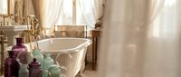 Luxury bathroom interior with vintage freestanding bathtub, elegant decor bottles, warm natural lighting and sophisticated home spa atmosphere.