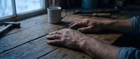 Elderly man hands resting on rustic wooden table with coffee mug in cozy indoor setting. Concept of aging, retirement, contemplation and peaceful moments.