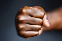Close-up view of dark-skinned male fist against blurred background showing strength, determination and power, dramatic lighting emphasizes texture of skin.