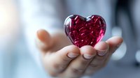 Female hand gently holding translucent red crystal heart against soft blurred background, symbolizing love, care, and tenderness. Romantic Valentine concept.