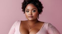 Young African American plus size woman with natural curly hair wearing pink lace top and delicate necklace against pink background, confident beauty portrait.