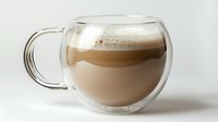 Layered coffee drink with milk foam in modern double wall glass cup on white background, elegant beverage presentation for cafe and restaurant menus.