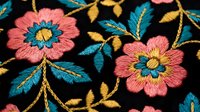 Colorful embroidered floral pattern with pink flowers and teal leaves on black fabric background for textile design and fashion applications.