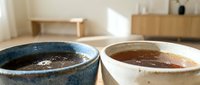 Two ceramic coffee cups with freshly brewed espresso on wooden table in modern minimalist kitchen interior with natural lighting and warm atmosphere.