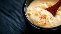 Creamy cheese sauce in black bowl with wooden spoon, melted cheddar for nachos, pasta or cooking recipes on dark background.