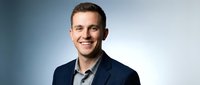 Young professional businessman smiling confidently in navy suit jacket against gradient background for corporate headshot and business marketing materials.