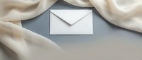 White envelope on gray background with flowing cream silk fabric creating elegant frame for luxury correspondence and wedding invitations.